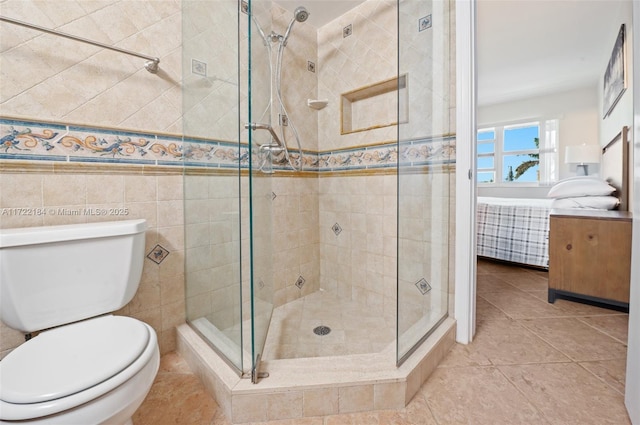 bathroom featuring tile patterned floors, toilet, a shower with shower door, and tile walls