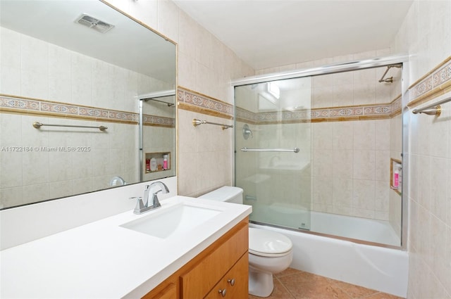 full bathroom featuring vanity, bath / shower combo with glass door, tile patterned flooring, toilet, and tile walls