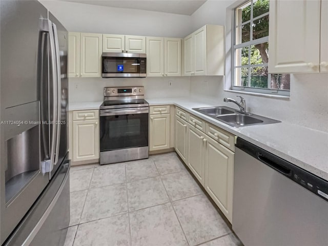 kitchen featuring cream cabinets, sink, light tile patterned floors, and stainless steel appliances