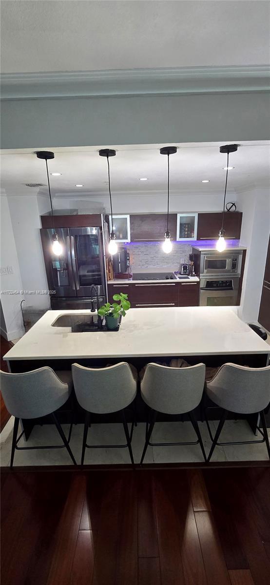 kitchen featuring hanging light fixtures, dark wood-type flooring, a kitchen breakfast bar, and appliances with stainless steel finishes