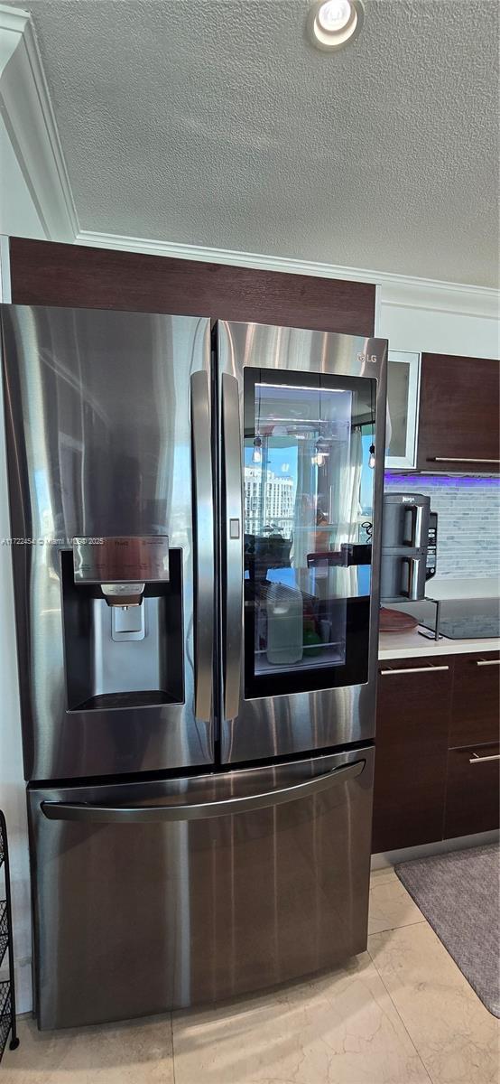 kitchen with crown molding, dark brown cabinets, stainless steel fridge, and a textured ceiling