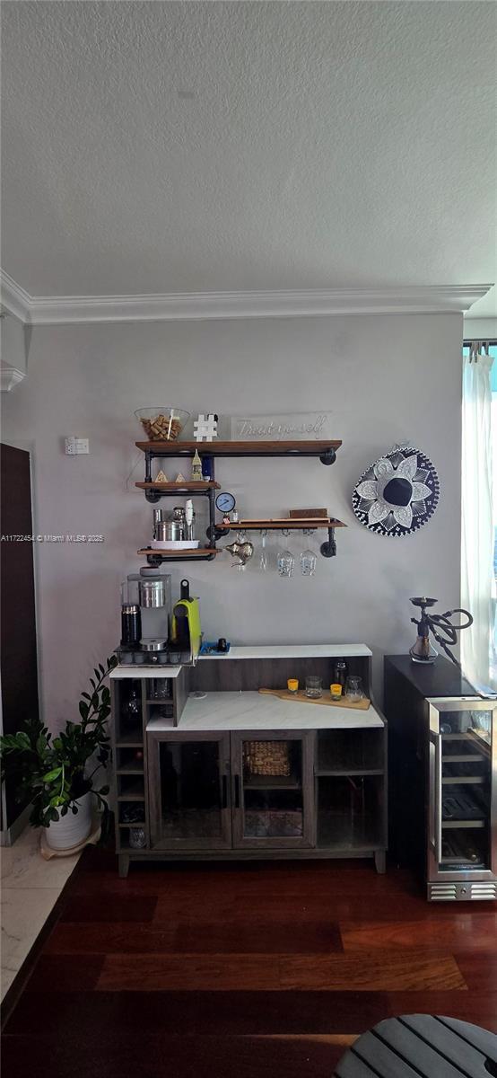 bar with dark wood-type flooring, ornamental molding, and a textured ceiling