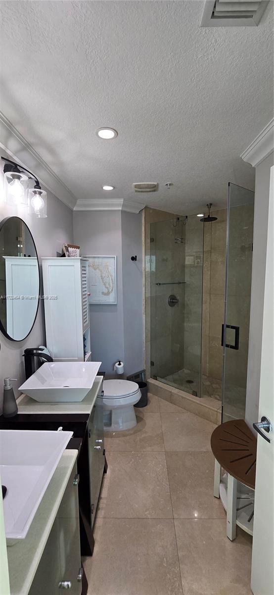 bathroom with crown molding, vanity, a textured ceiling, toilet, and walk in shower