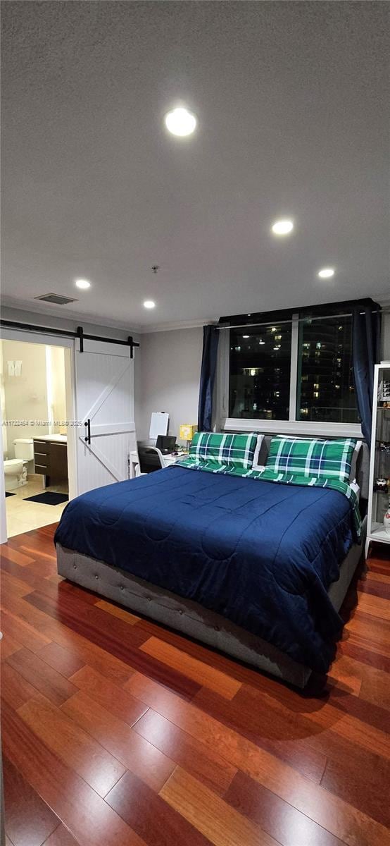 bedroom with hardwood / wood-style flooring, ensuite bathroom, a barn door, and a textured ceiling