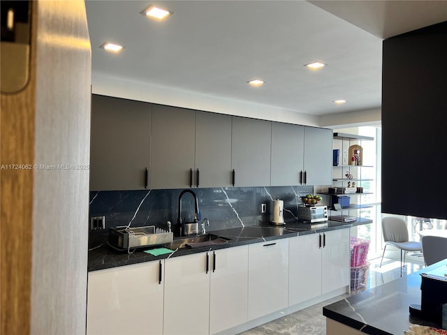 kitchen with backsplash, white cabinetry, dark stone countertops, and sink