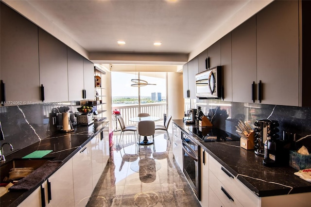 kitchen featuring tasteful backsplash, dark stone counters, stainless steel oven, black electric cooktop, and hanging light fixtures