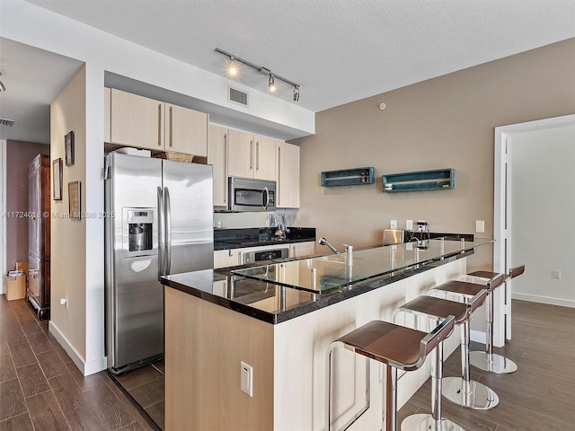 kitchen with dark stone counters, a textured ceiling, appliances with stainless steel finishes, cream cabinetry, and a breakfast bar area