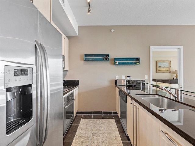 kitchen with track lighting, a textured ceiling, stainless steel appliances, dark tile patterned floors, and sink