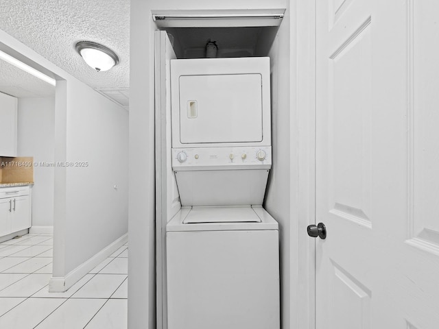 washroom featuring a textured ceiling, stacked washer and dryer, and light tile patterned flooring