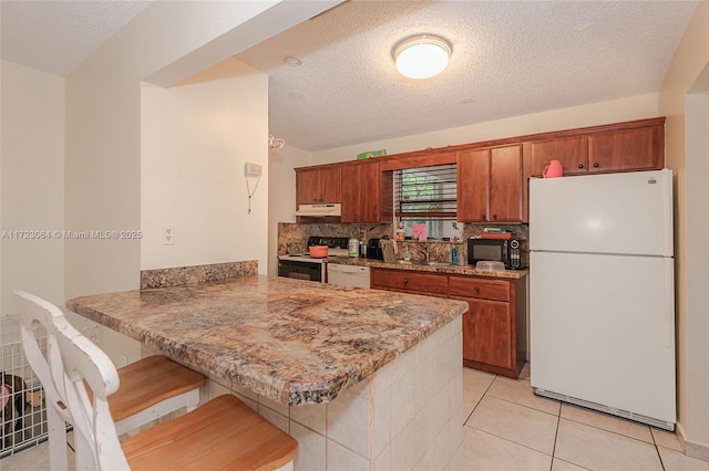 kitchen featuring a kitchen bar, kitchen peninsula, light tile patterned floors, and white appliances