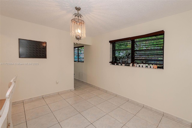 empty room with light tile patterned floors, a textured ceiling, and a chandelier