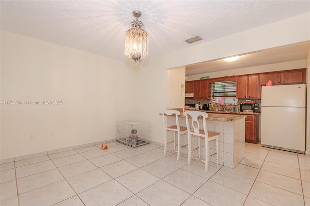 kitchen featuring hanging light fixtures, an inviting chandelier, white fridge, a textured ceiling, and a breakfast bar area