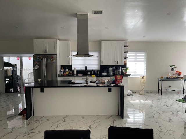 kitchen featuring white cabinetry, a kitchen breakfast bar, backsplash, stainless steel fridge, and exhaust hood