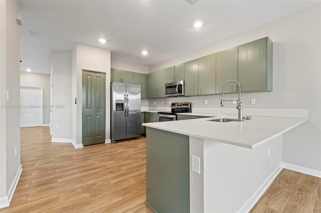 kitchen with kitchen peninsula, sink, appliances with stainless steel finishes, and green cabinetry