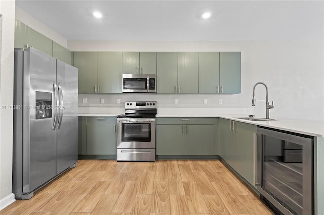 kitchen with stainless steel appliances, beverage cooler, sink, light hardwood / wood-style flooring, and green cabinets