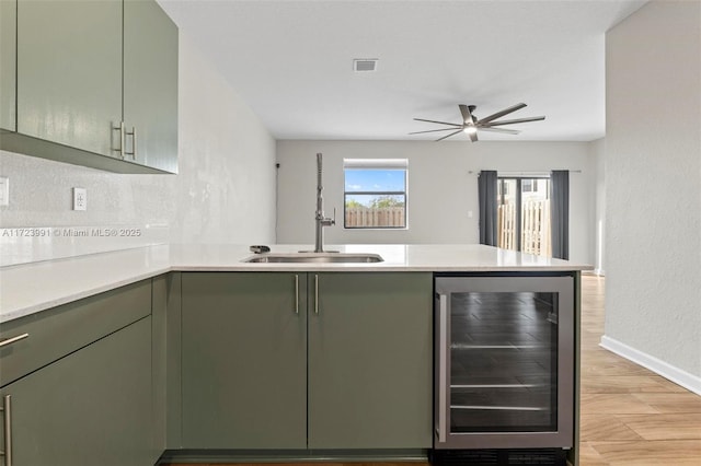 kitchen with ceiling fan, sink, beverage cooler, green cabinets, and kitchen peninsula