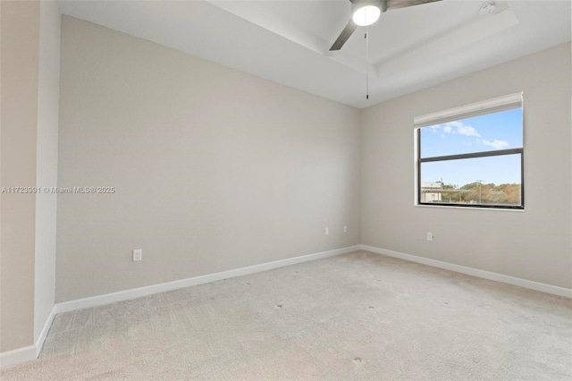 spare room with a raised ceiling, light carpet, and ceiling fan