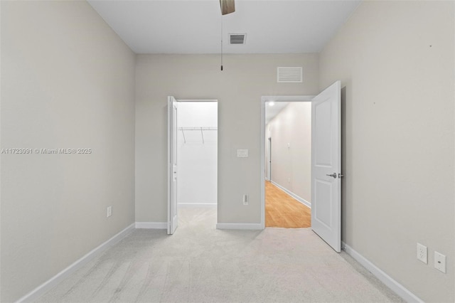 unfurnished bedroom featuring a walk in closet, ceiling fan, a closet, and light carpet