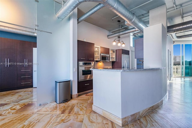 kitchen with dark brown cabinetry, light stone countertops, a high ceiling, decorative light fixtures, and appliances with stainless steel finishes