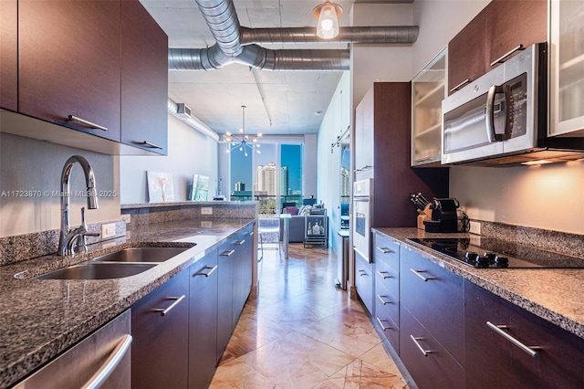 kitchen with appliances with stainless steel finishes, dark brown cabinetry, dark stone counters, and sink