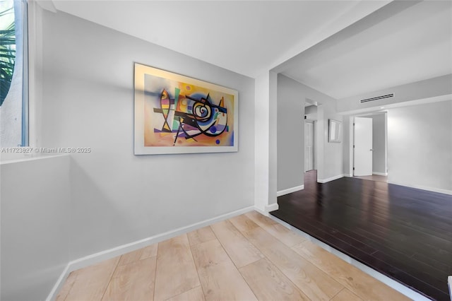 hall with baseboards, visible vents, and wood finished floors