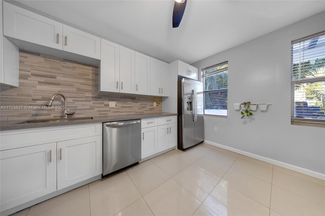 kitchen featuring light tile patterned flooring, white cabinets, appliances with stainless steel finishes, a sink, and backsplash