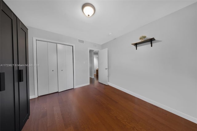 unfurnished bedroom with a closet, dark wood-style flooring, visible vents, and baseboards