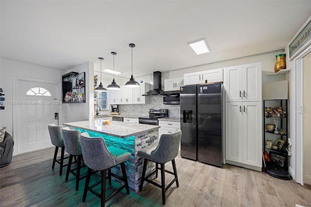 kitchen featuring wall chimney exhaust hood, decorative light fixtures, white cabinets, appliances with stainless steel finishes, and sink