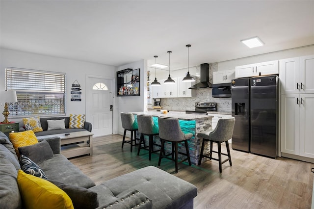 kitchen featuring wall chimney range hood, a breakfast bar, stainless steel electric range, white cabinets, and fridge with ice dispenser