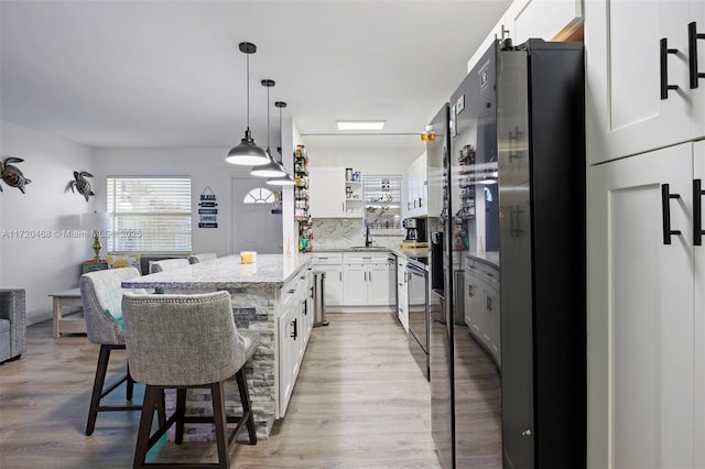 kitchen with light stone counters, decorative light fixtures, a kitchen island, a breakfast bar area, and white cabinetry