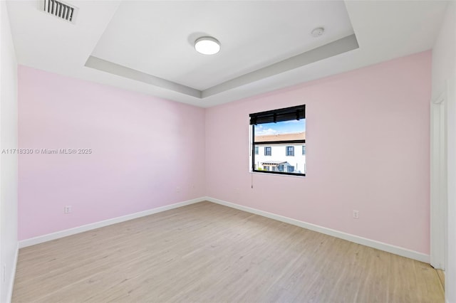 empty room featuring a raised ceiling and light wood-type flooring