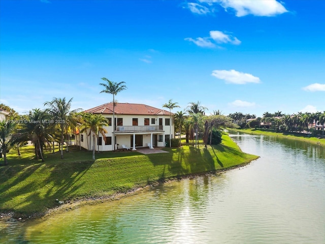 rear view of property featuring a lawn, a balcony, a water view, and a patio