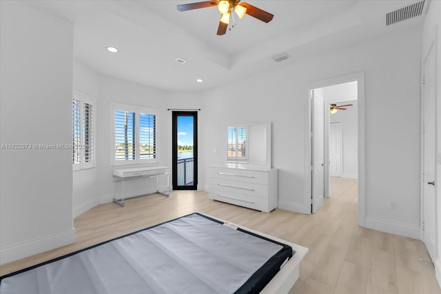 unfurnished bedroom with ceiling fan, a tray ceiling, access to exterior, and light wood-type flooring