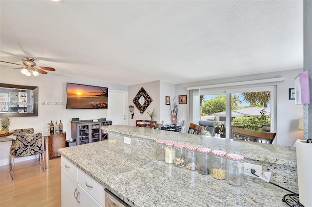 kitchen with light stone counters, white cabinets, ceiling fan, and light hardwood / wood-style flooring