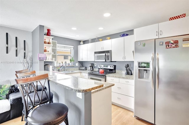 kitchen with a breakfast bar area, appliances with stainless steel finishes, light stone counters, sink, and white cabinetry