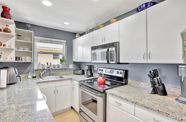 kitchen featuring appliances with stainless steel finishes, white cabinetry, light stone counters, and sink