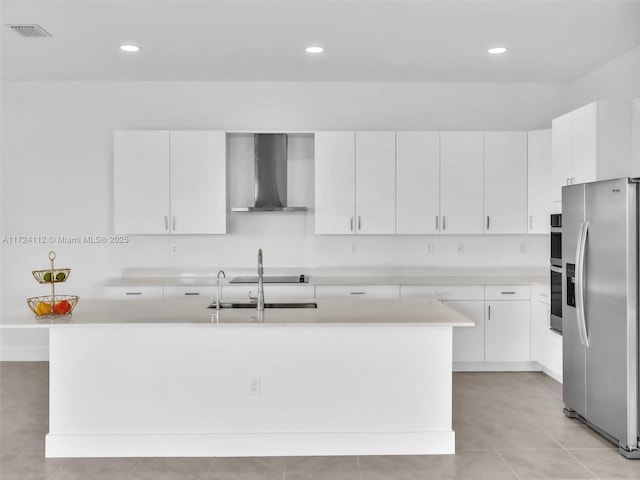 kitchen featuring stainless steel refrigerator with ice dispenser, wall chimney range hood, white cabinetry, sink, and a kitchen island with sink