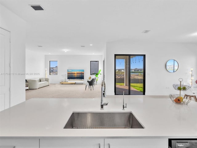 kitchen featuring carpet, dishwashing machine, white cabinetry, and sink