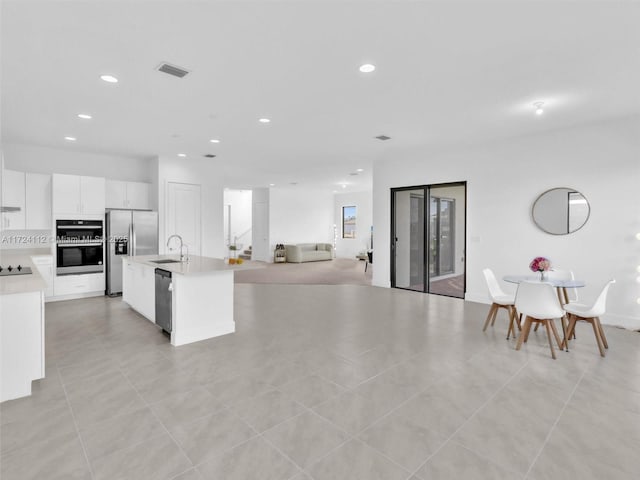 kitchen with sink, light tile patterned floors, an island with sink, stainless steel appliances, and white cabinets