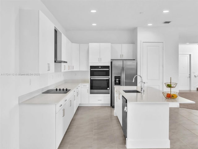 kitchen featuring white cabinetry, wall chimney range hood, stainless steel appliances, an island with sink, and sink