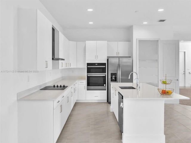 kitchen with wall chimney range hood, sink, white cabinetry, a kitchen island with sink, and appliances with stainless steel finishes