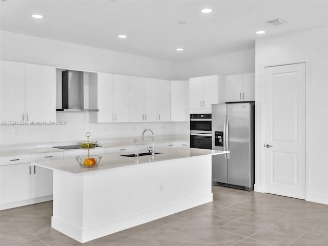 kitchen with wall chimney range hood, sink, a kitchen island with sink, stainless steel appliances, and white cabinets