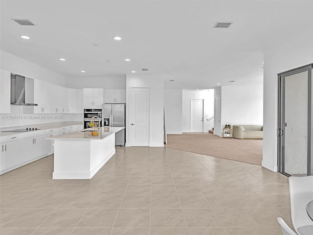 kitchen featuring light tile patterned floors, an island with sink, appliances with stainless steel finishes, wall chimney range hood, and white cabinets