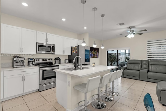 kitchen featuring decorative light fixtures, a center island with sink, white cabinets, appliances with stainless steel finishes, and sink