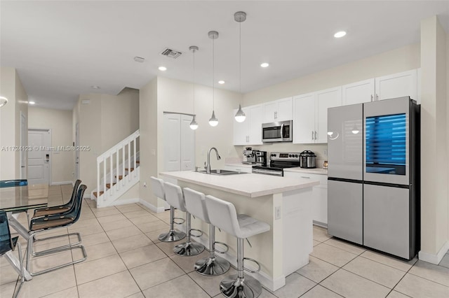 kitchen featuring a kitchen island with sink, appliances with stainless steel finishes, light tile patterned floors, sink, and decorative light fixtures