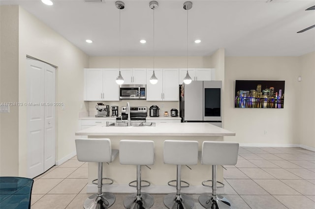 kitchen featuring hanging light fixtures, stainless steel appliances, a kitchen island with sink, light tile patterned flooring, and sink