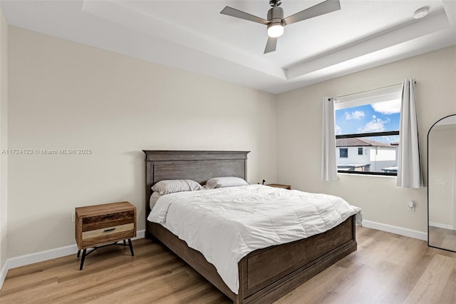 bedroom with ceiling fan, a tray ceiling, and wood-type flooring