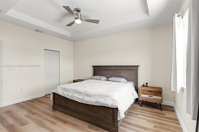 bedroom with a raised ceiling, a closet, ceiling fan, and light wood-type flooring