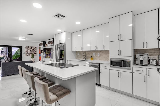 kitchen with sink, stainless steel appliances, a kitchen breakfast bar, decorative backsplash, and white cabinets