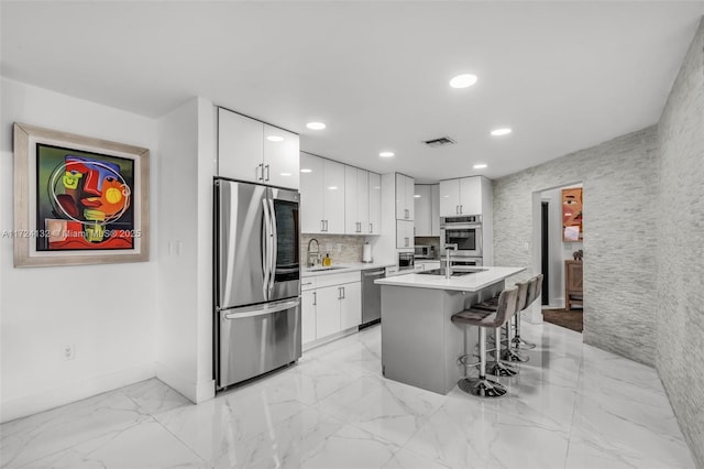 kitchen with appliances with stainless steel finishes, a breakfast bar, a kitchen island with sink, sink, and white cabinetry